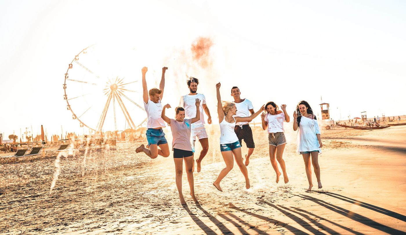 Happy friends group having fun at ferris wheel seaside - Summer vacations friendship concept with millenial guys and girls cheering at public beach - Warm sunset color tone with contrast filtered look